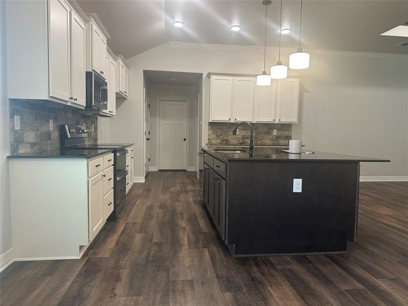 Kitchen featuring black range with electric stovetop, dark countertops, stainless steel microwave, decorative backsplash, and crown molding