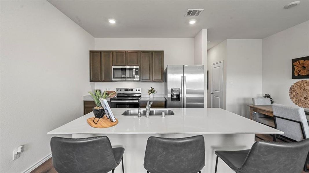 Kitchen featuring stainless steel appliances, dark brown cabinets, a center island with sink, a breakfast bar, and recessed lighting