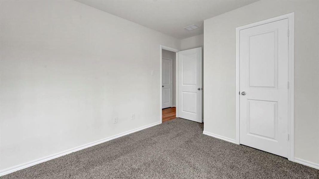 Gray carpeted flooring with white baseboards, white walls, and a white paneled door with a brushed nickel knob