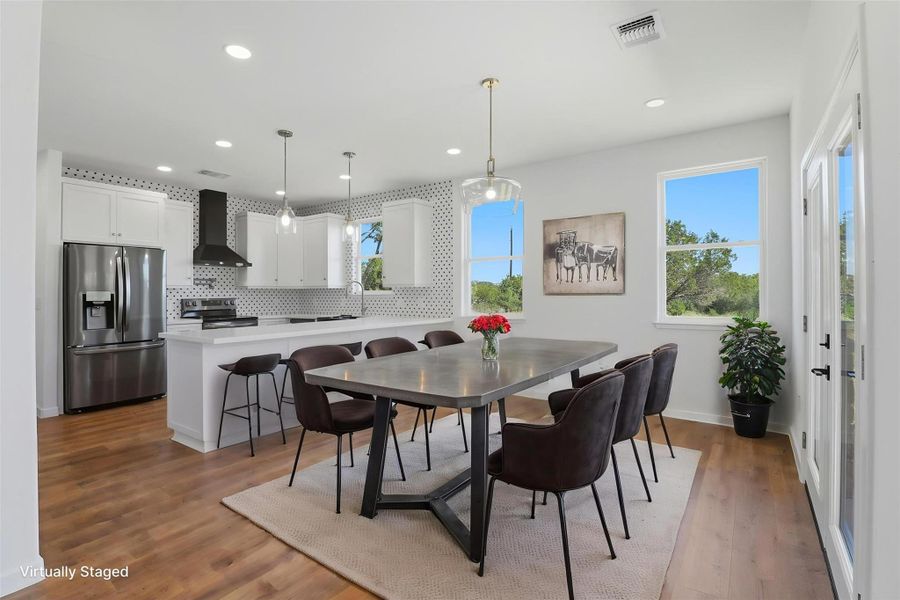 Open-concept kitchen and dining area featuring wood-finish flooring, white cabinetry, a large kitchen island with bar seating, stainless steel appliances, and a full-height tile backsplash Open-concept kitchen and dining area featuring wood-finish flooring, white cabinetry, a large kitchen island with bar seating, stainless steel appliances, and a full-height tile backsplash