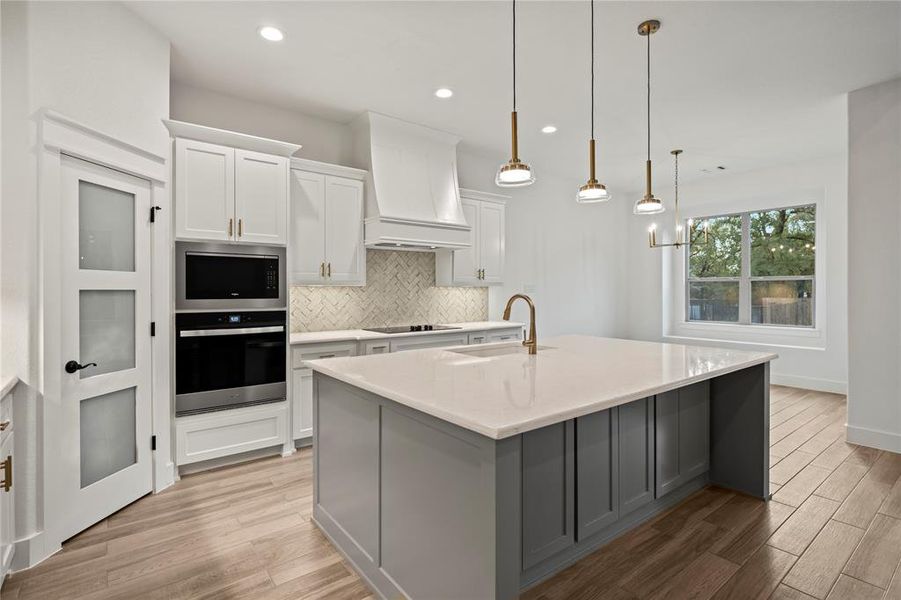 Kitchen with backsplash, white cabinets, appliances with stainless steel finishes, gray cabinetry, and light wood-type flooring