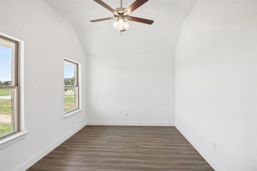 Empty room featuring vaulted ceiling, dark hardwood / wood-style flooring, and a wealth of natural light