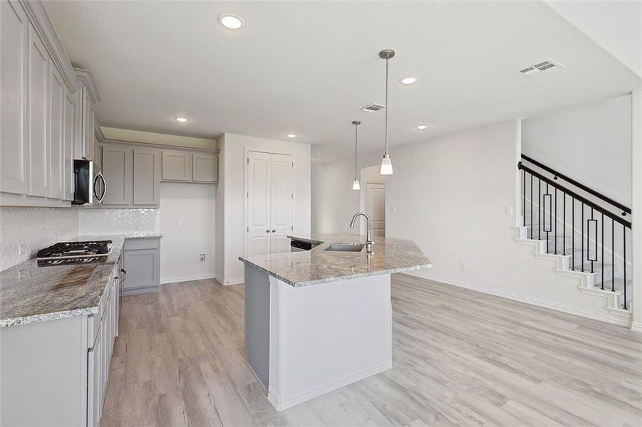 Kitchen featuring a kitchen island with sink, light hardwood / wood-style flooring, sink, light stone countertops, and pendant lighting