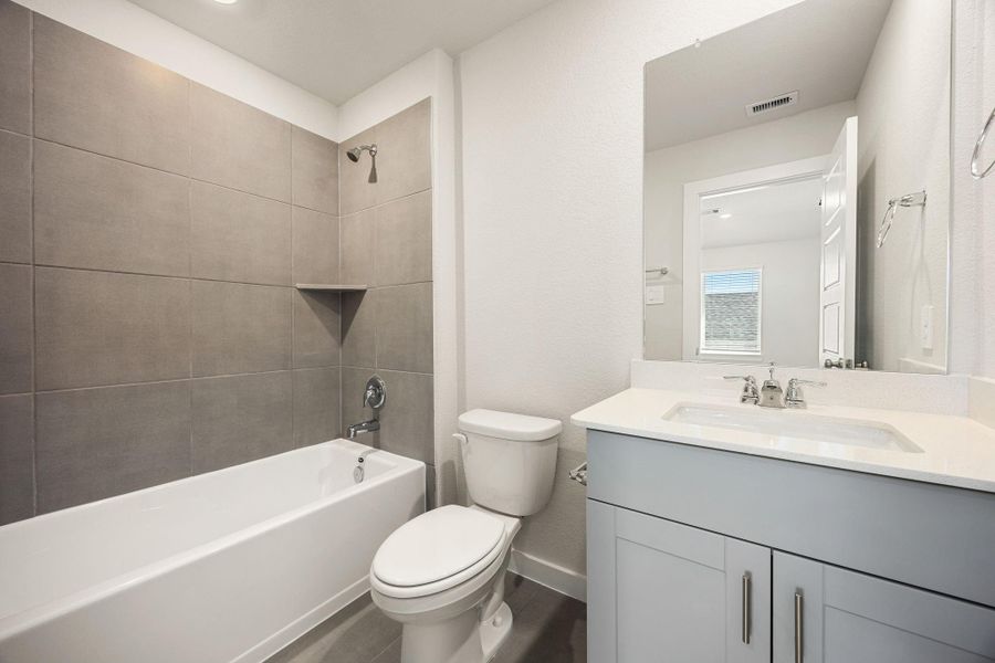 The ensuite bathroom offers tile flooring, a bath/shower combination with a stylish tile surround, rich stained wood cabinetry, elegant light countertops, a mirror, and sleek fixtures with modern finishes. The ensuite bathroom offers tile flooring, a bath/shower combination with a stylish tile surround, rich stained wood cabinetry, elegant light countertops, a mirror, and sleek fixtures with modern finishes.