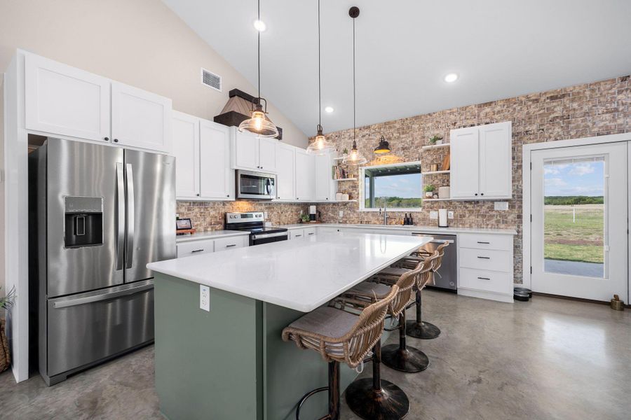 Kitchen featuring stainless steel appliances, open shelves, a kitchen island, a breakfast bar, and pendant lighting