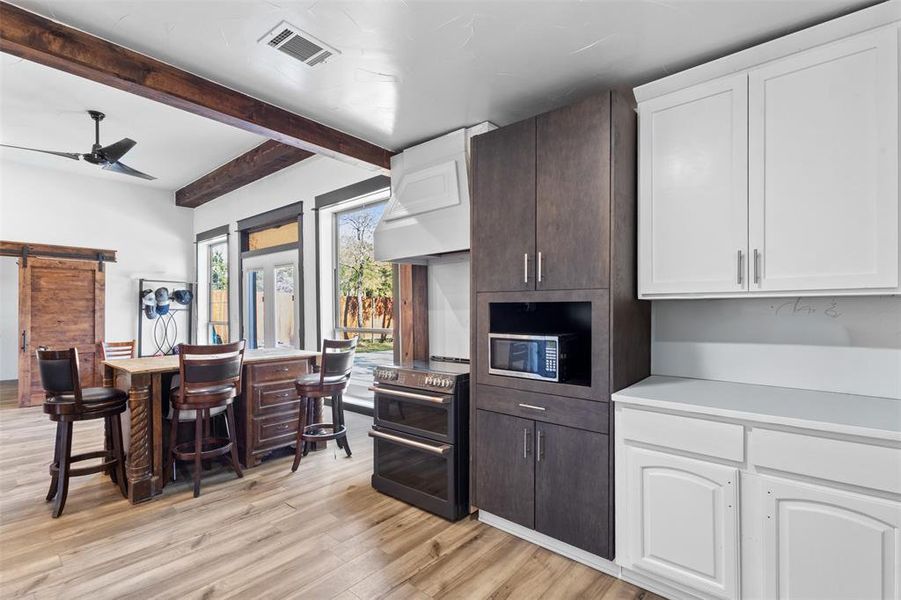 Kitchen featuring a barn door, light countertops, beam ceiling, dark brown cabinets, and light wood-type flooring Kitchen featuring a barn door, light countertops, beam ceiling, dark brown cabinets, and light wood-type flooring