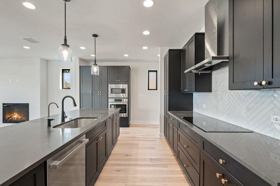 Kitchen featuring wall chimney range hood, appliances with stainless steel finishes, dark stone counters, and recessed lighting