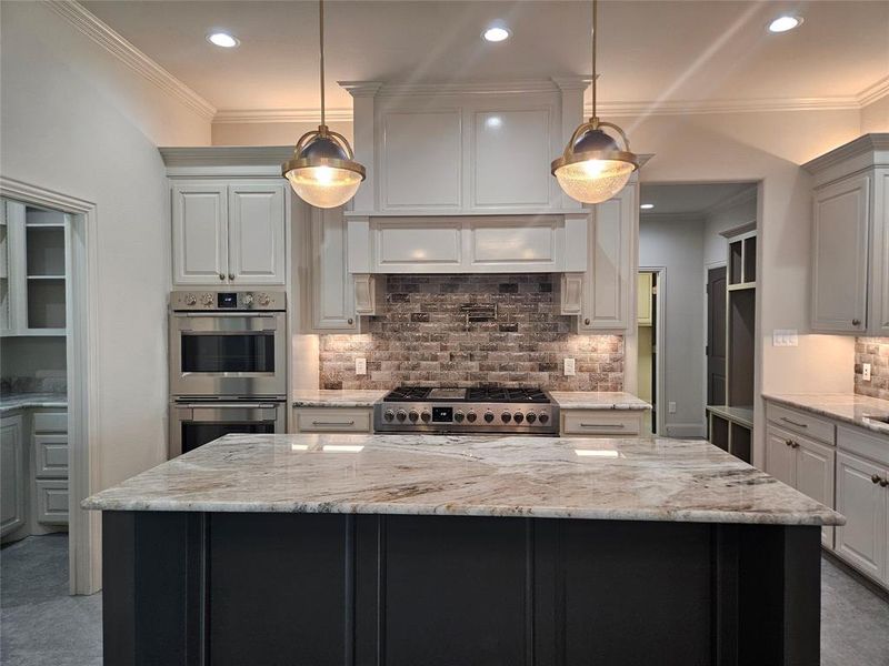 Kitchen featuring a kitchen island, light stone countertops, stainless steel appliances, and decorative light fixtures