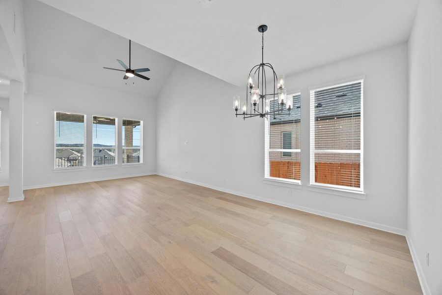 Empty room featuring a ceiling fan, light wood finished floors, a chandelier, and lofted ceiling Empty room featuring a ceiling fan, light wood finished floors, a chandelier, and lofted ceiling