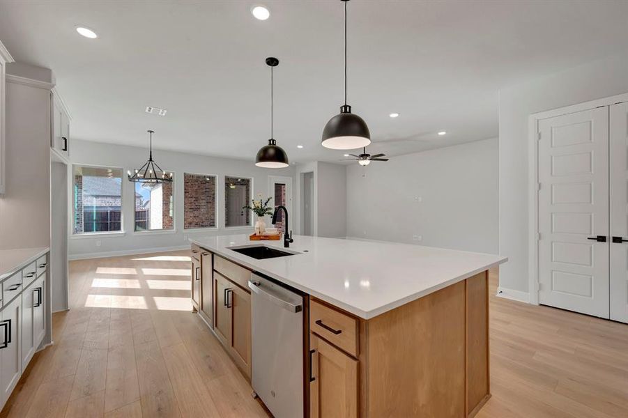 Dual tone kitchen featuring suspended lighting, a kitchen island with sink, stainless steel dishwasher, light wood-type flooring, and open floor plan