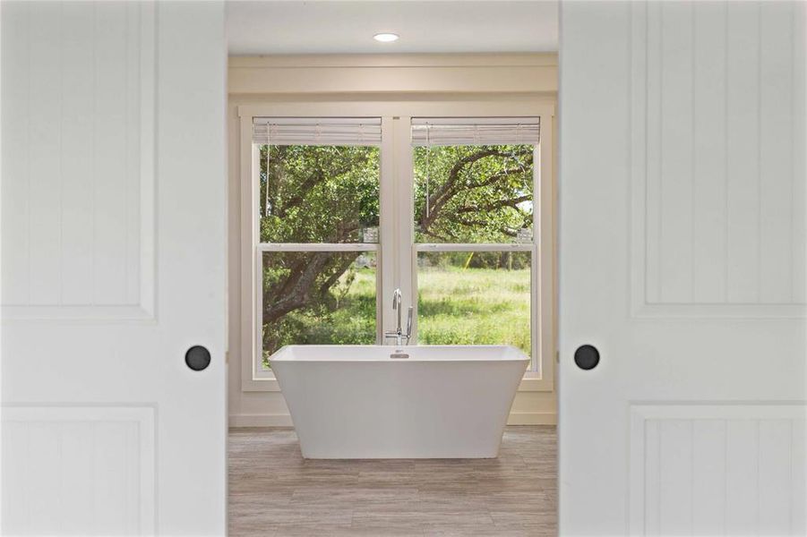Freestanding soaking tub centered before a large window with natural surroundings