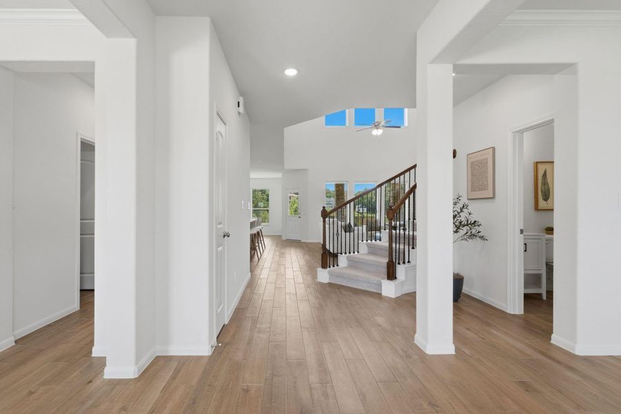 This photo showcases a bright, open entryway with elegant wooden tile flooring and a curved staircase. The space features high ceilings and large windows, providing plenty of natural light. The layout offers a modern and inviting atmosphere.