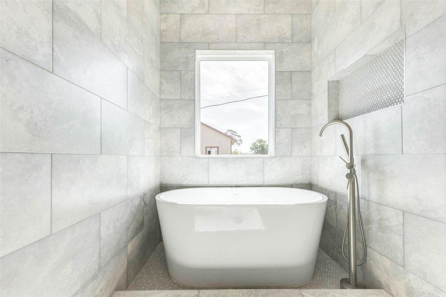 A freestanding soaking tub is centered beneath a large privacy window within a fully tiled wet area.