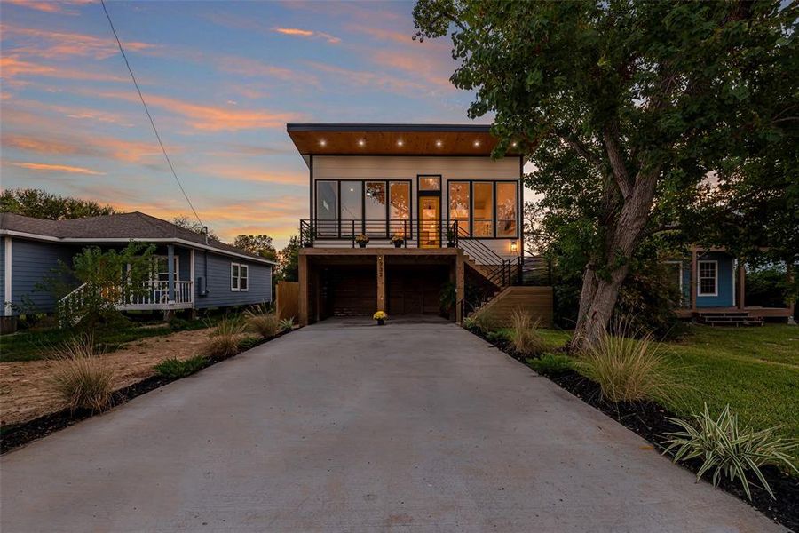 Modern two-story home with expansive windows, an elevated deck, and a spacious driveway, nestled in Bay Front La Porte surrounded by mature trees.