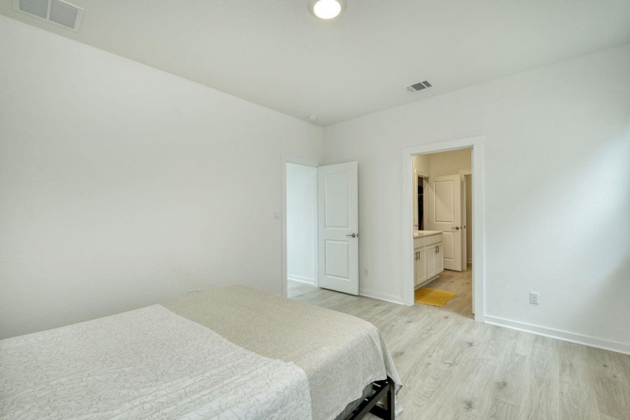 Bedroom featuring light wood-type flooring, visible vents, connected bathroom, and baseboards