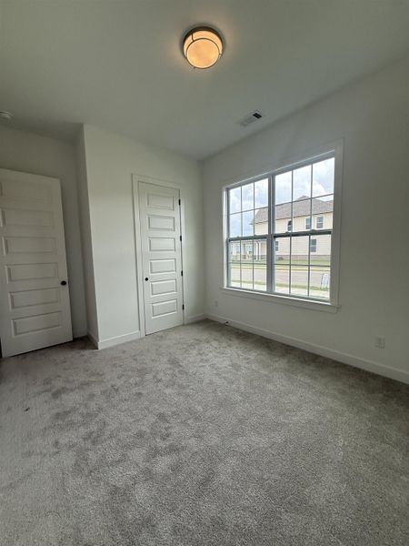 Spacious room featuring neutral carpeting, a large window, white trim, two white paneled doors, and a ceiling-mounted light fixture