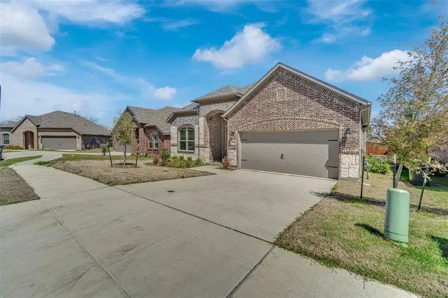 French country inspired facade featuring an attached garage, driveway, stone siding, brick siding, and a front lawn