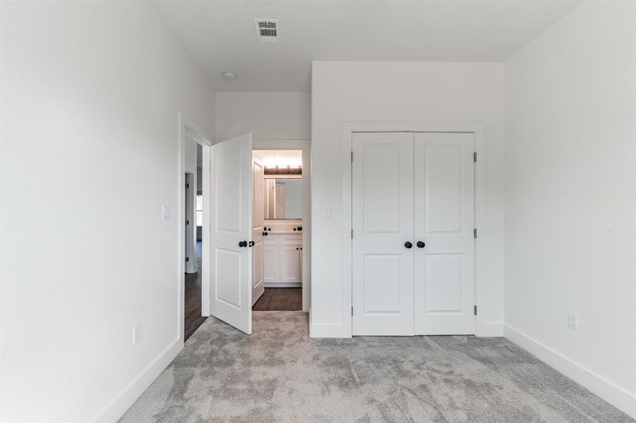 Unfurnished bedroom featuring light colored carpet, ensuite bath, and a closet