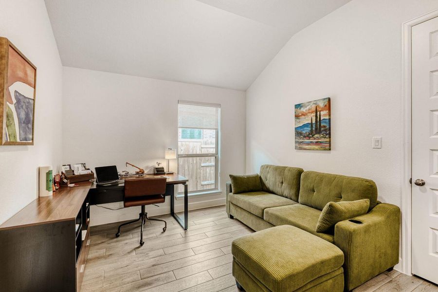 Home office with light wood-style floors and lofted ceiling