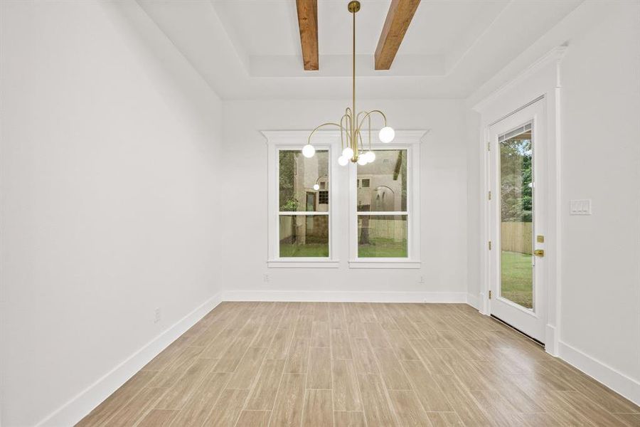 Recessed ceiling with exposed wood beams, modern brass chandelier, and wood-finish tile flooring
