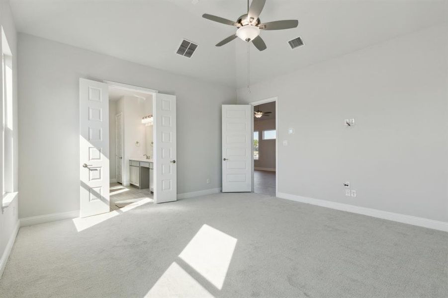 Unfurnished bedroom with ensuite bathroom, ceiling fan, and light colored carpet