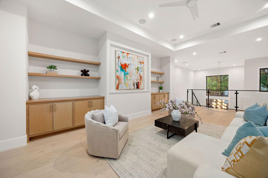 This inviting lounge area is designed for both comfort and connection, featuring a well-balanced layout and warm finishes throughout. Natural light enhances the airy feel, while clean lines keep the space modern. The highlight of this room is the custom built-in shelving paired with statement artwork, creating a striking focal wall that adds personality and architectural interest.