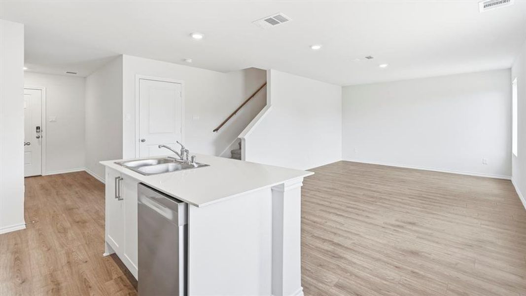 Kitchen featuring dishwasher, a center island with sink, light wood finished floors, white cabinetry, and open floor plan