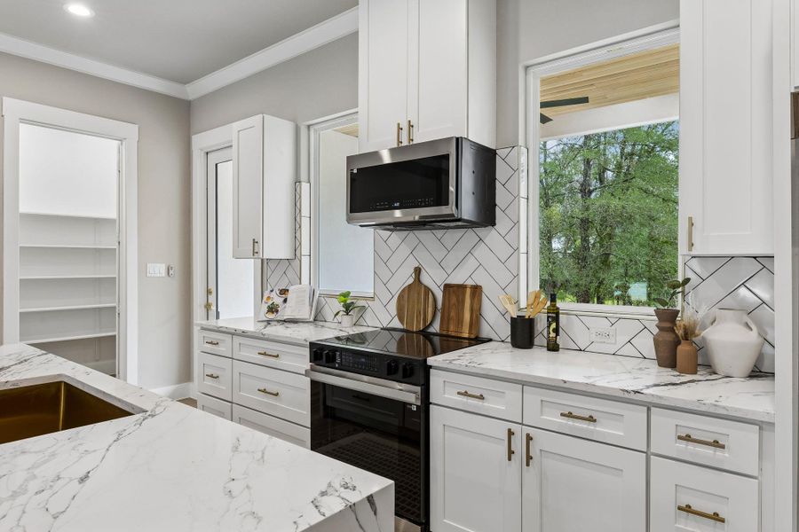 White cabinetry, elegant stone countertops, and herringbone tile create a crisp, inviting culinary space.