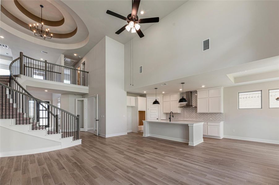 Unfurnished living room with a tray ceiling, recessed lighting, a towering ceiling, a chandelier, and stairway