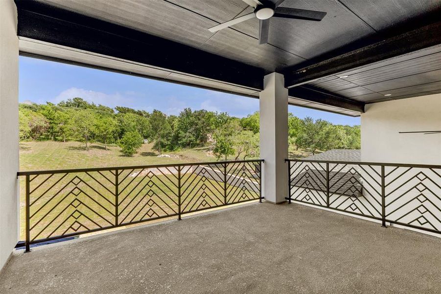 Spacious covered balcony featuring a dark wood-finish ceiling, ceiling fan, and decorative geometric metal railings