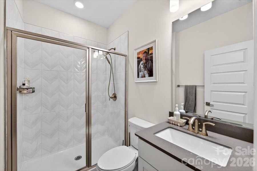 Guest bathroom on the main level with tile-surround shower, glass shower doors, tiled floor, and quartz countertop vanity.