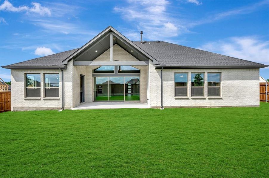 Expansive backyard featuring a lush lawn, white brick exterior, dark grey shingle roof, large sliding glass doors, and a covered patio area