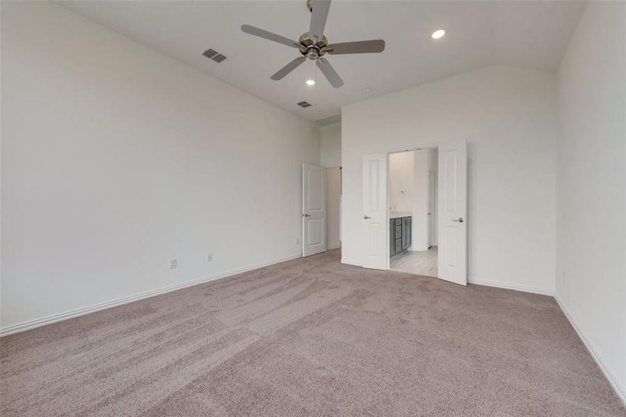 Unfurnished bedroom featuring ceiling fan, light colored carpet, lofted ceiling, and ensuite bath