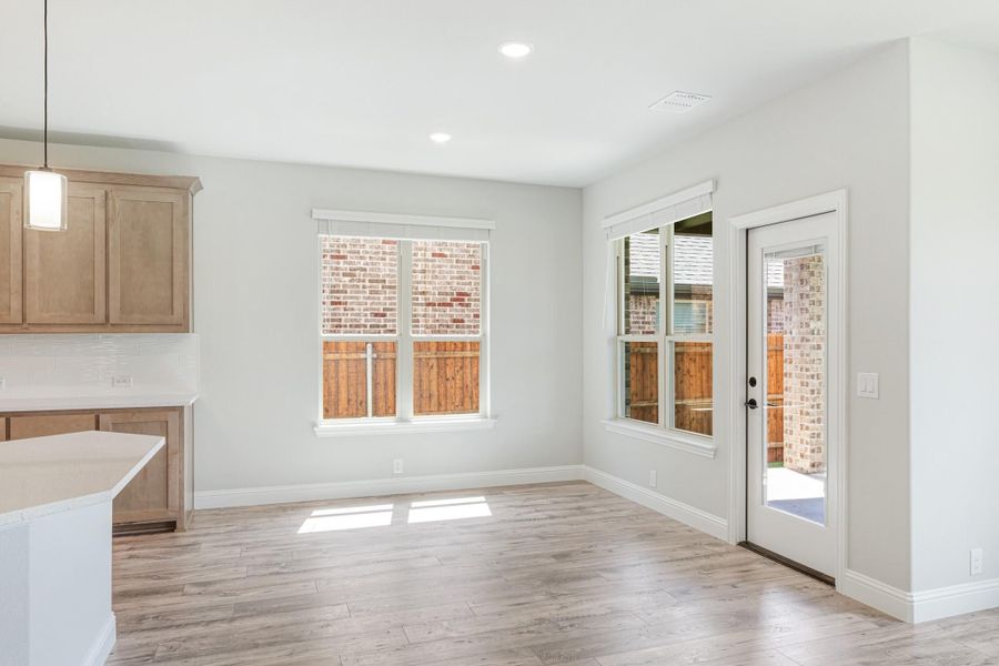 Bright dining area with light wood floors, back door, and windows overlooking a wood fence