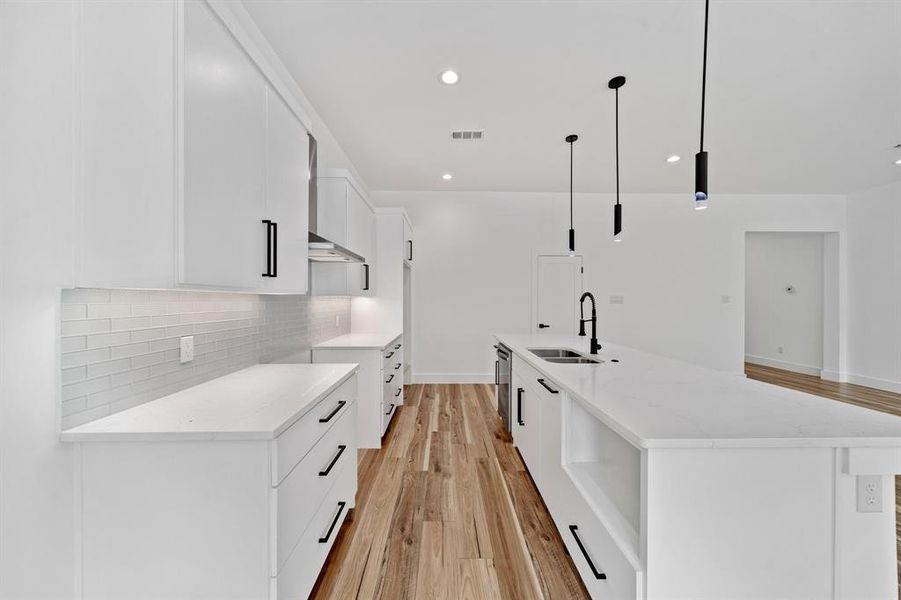 Kitchen with light hardwood / wood-style flooring, an island with sink, sink, pendant lighting, and white cabinets