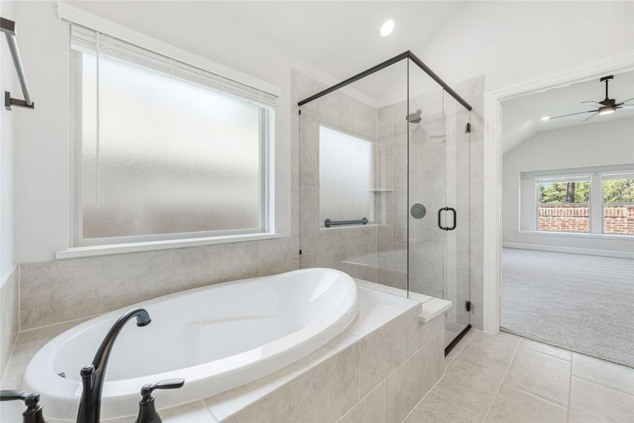 Master bathroom with soaking tub, glass-enclosed shower, and tile floors open to carpeted bedroom