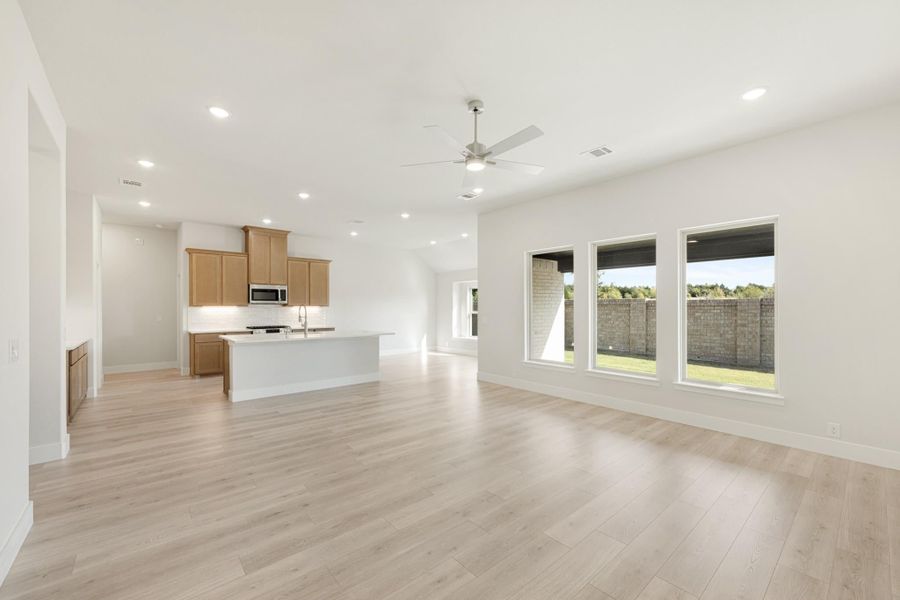 Open living area with light wood floors, ceiling fan, and kitchen with island and wood cabinets in background Open living area with light wood floors, ceiling fan, and kitchen with island and wood cabinets in background