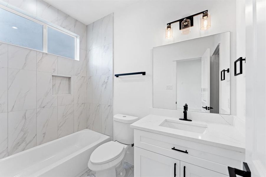 This modern bathroom features a sleek design with white marble tiles, a built-in bathtub, and a large vanity with a stylish black faucet. It also includes a large mirror and contemporary lighting, creating a bright and inviting space.