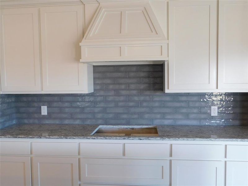 Kitchen with premium range hood, tasteful backsplash, light stone counters, and white cabinets