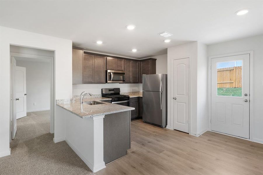 Kitchen with sink, appliances with stainless steel finishes, dark brown cabinets, light stone counters, and kitchen peninsula