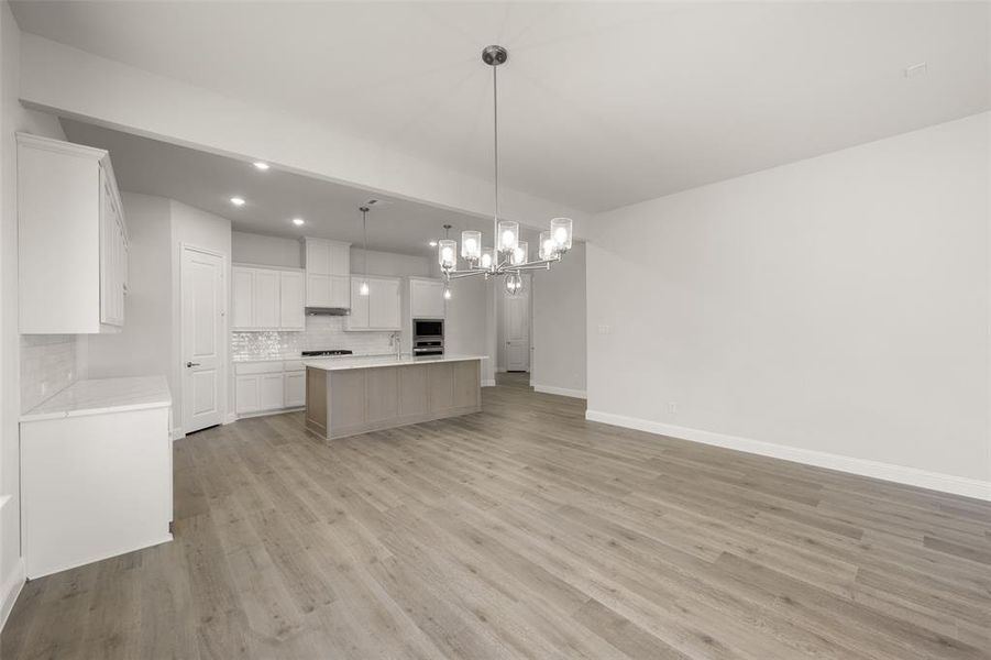 Kitchen with tasteful backsplash, open floor plan, light wood-type flooring, light countertops, and a chandelier Kitchen with tasteful backsplash, open floor plan, light wood-type flooring, light countertops, and a chandelier