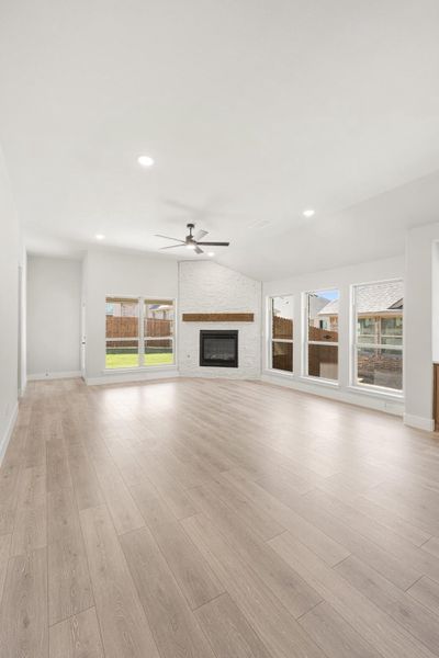 Open living room with light wood floors, white brick fireplace, ceiling fan, and large windows