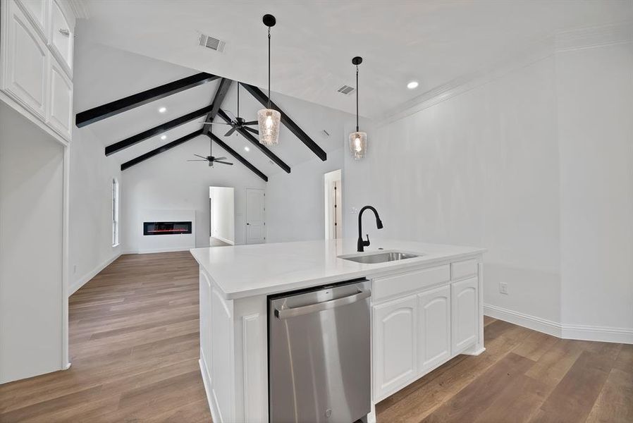 Kitchen featuring white cabinets, a glass covered fireplace, stainless steel dishwasher, light wood finished floors, and beam ceiling
