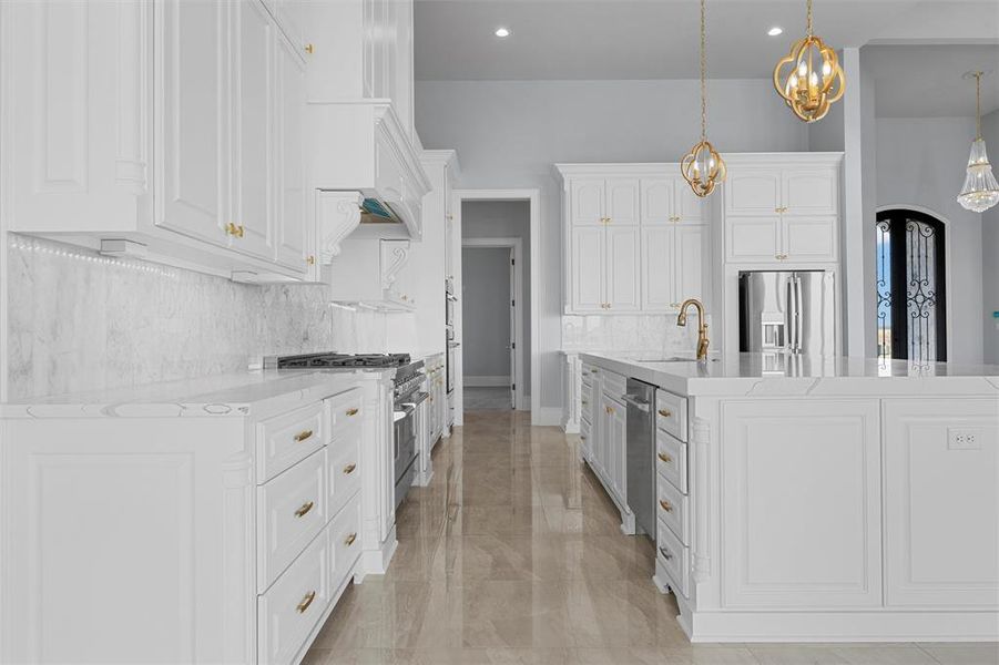 Kitchen featuring white cabinetry, light stone countertops, decorative backsplash, a large island with sink, and stainless steel appliances Kitchen featuring white cabinetry, light stone countertops, decorative backsplash, a large island with sink, and stainless steel appliances