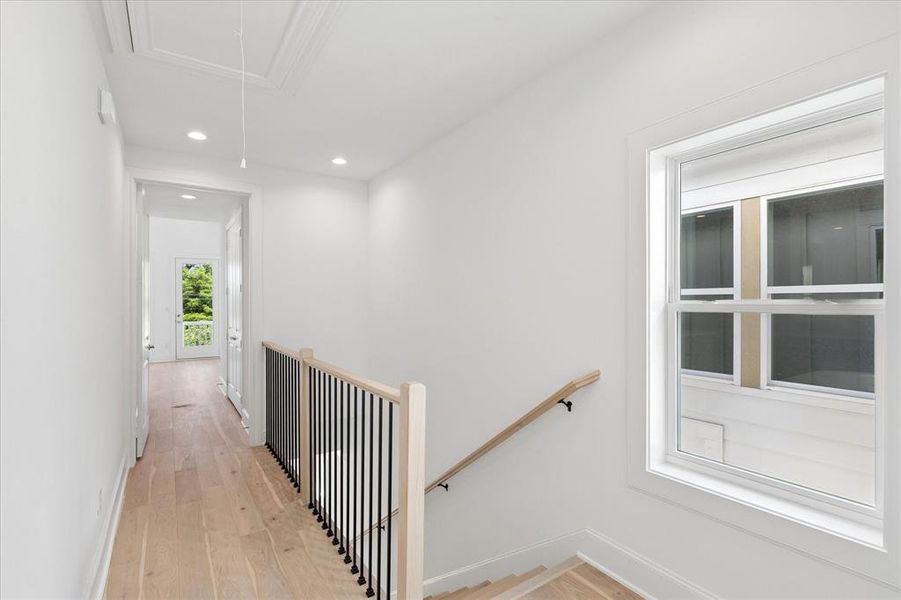 Upper-level hallway featuring light wood-finish flooring, recessed lighting, and a contemporary railing with black balusters and a wood-finish handrail