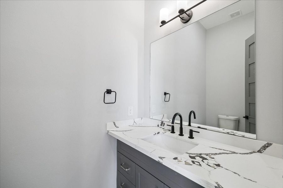 Powder room offering a quartz countertop with black hardware, and a full-size mirror that enhances the room’s brightness.