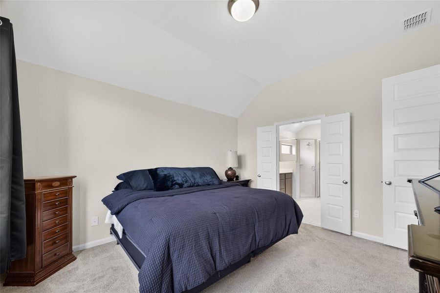 This photo showcases a cozy primary bedroom with neutral walls and carpet, Double doors lead into a bright en-suite bathroom, adding convenience and privacy. This photo showcases a cozy primary bedroom with neutral walls and carpet, Double doors lead into a bright en-suite bathroom, adding convenience and privacy.