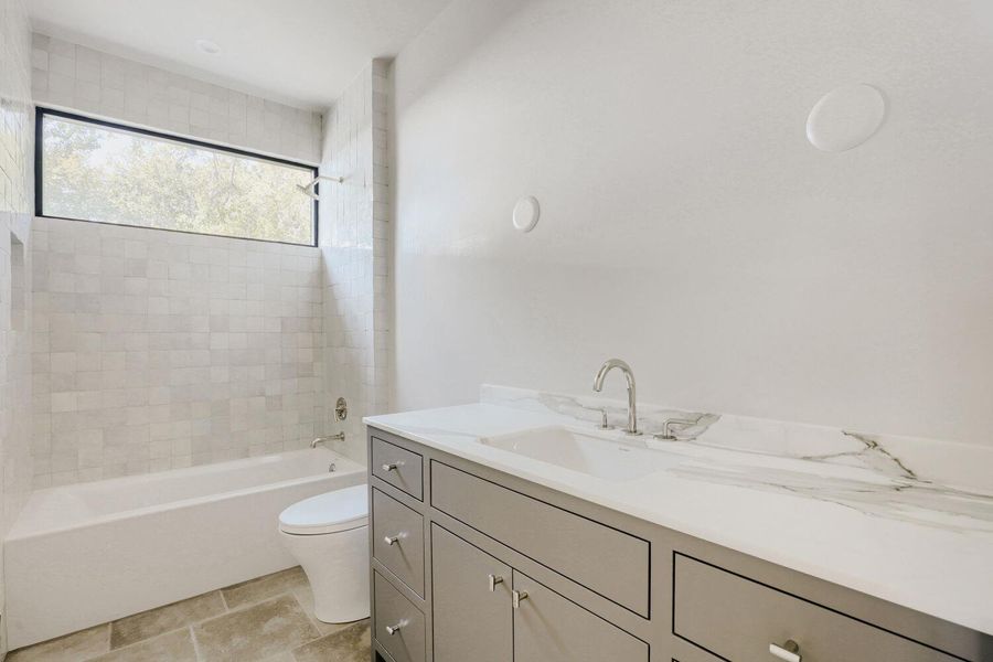 A well-appointed bathroom features a single vanity with stone counters and a tub/shower combination, complemented by tile flooring.