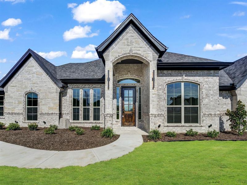 Property entrance featuring stone siding, brick siding, and a lawn Property entrance featuring stone siding, brick siding, and a lawn