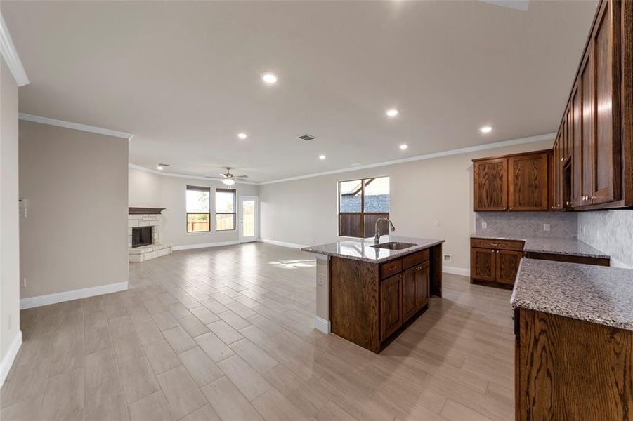 Kitchen featuring light stone countertops, sink, a stone fireplace, and an island with sink